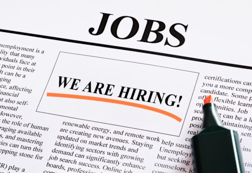 A close-up of a newspaper job ad with "WE ARE HIRING!" highlighted in bold text inside a box, an orange marker beside it, and the word "JOBS" at the top—perfectly illustrating PERM Labor Certification or labor certification processes.